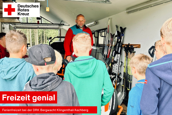 Kinder stehen mit dem Rücken zum Fotografen und ein Kamerad der Bergwacht Klingenthal/Aschberg erklärt den Fuhrpark in der Garage.